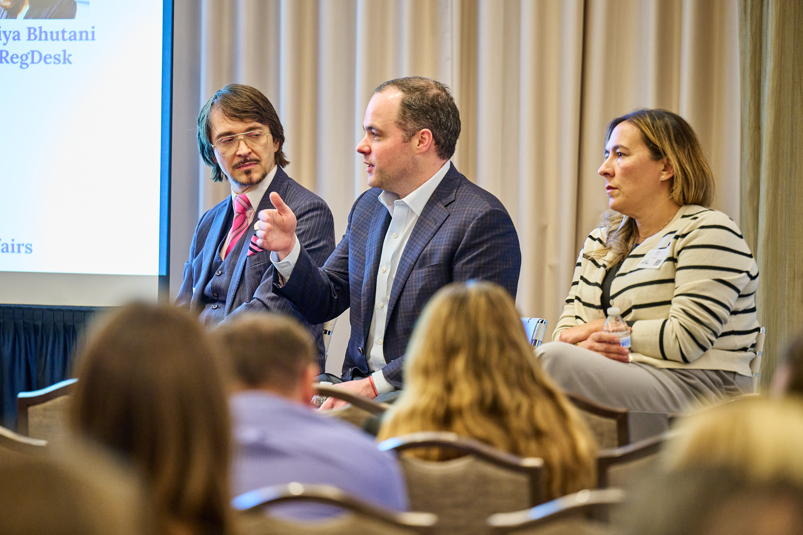 Healthcare Innovation Conference Panel - Global Health Innovators Summit conference panel discussion featuring three healthcare professionals seated at a panel table. Shows a man with glasses and mustache in a pinstripe suit on the left, a man in gray suit in the middle, and a woman in striped top on the right. Professional conference setting with engaged audience members and OMNI Nashville branding visible in the background.